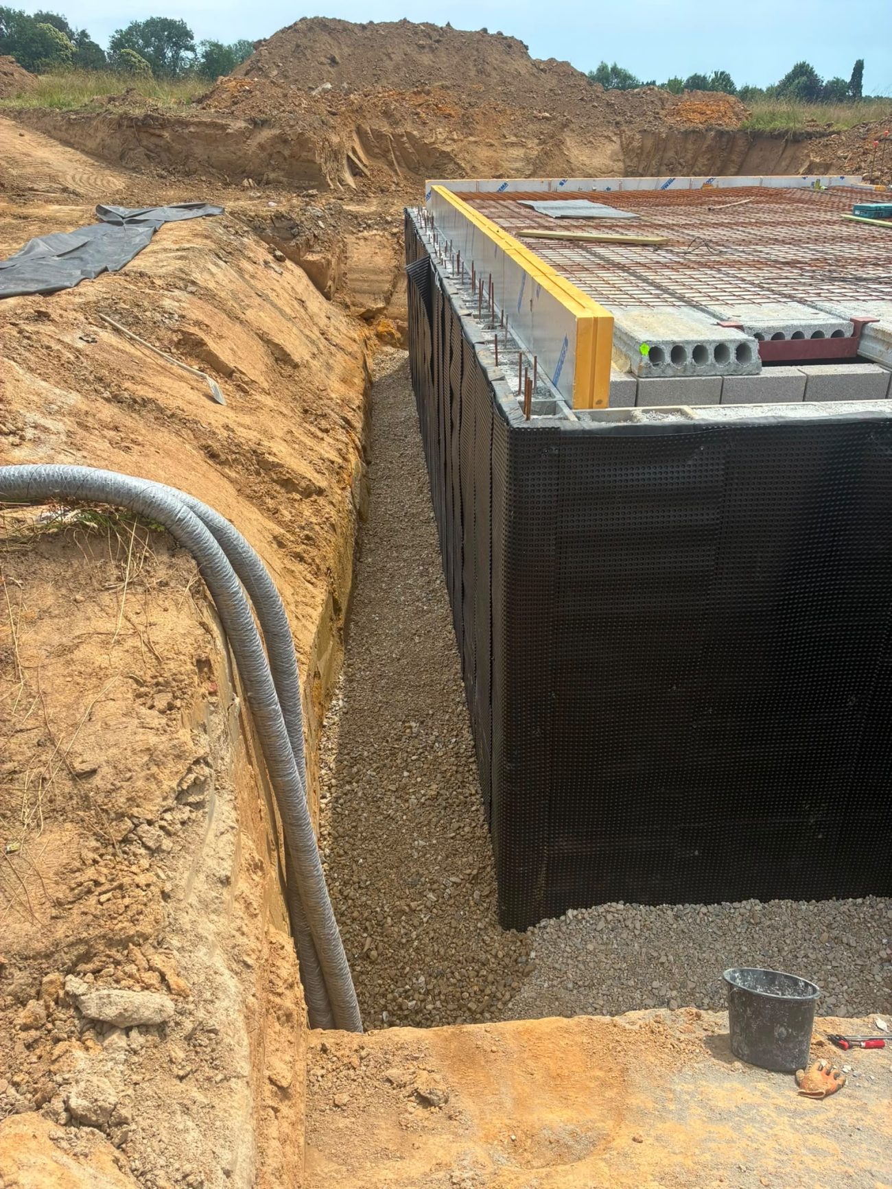 Étanchéité verticale, membrane de protection et drainage en pied de mur, avant remblai. Aucun de ces ouvrages ne sera visible une fois la maison terminée.